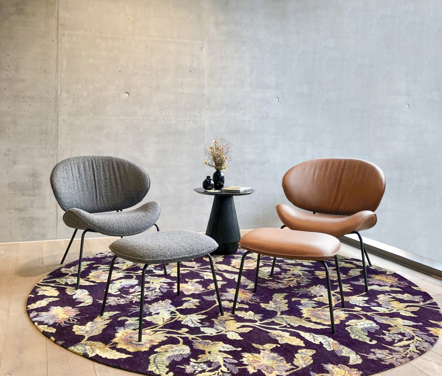 Grauer und brauner Alvaro Lounge Sessel mit Ottomane vor Betonwand auf buntem Teppich