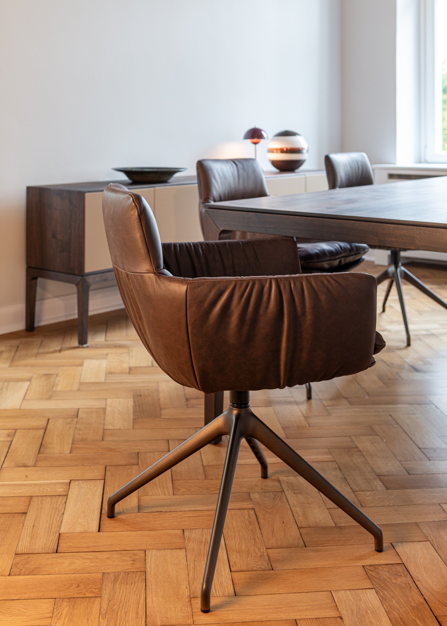 FAYE CASUAL chair in brown leather on a swivel base at the ASCO Aereo table in walnut
